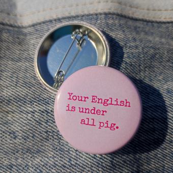Ansteckbutton Your English is under all pig auf Jeans mit Rückseite